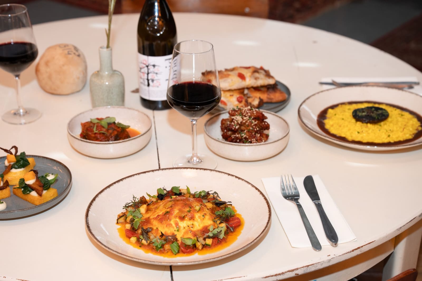 A table set with ravioli, antipasti, saffron risotto and red wine
