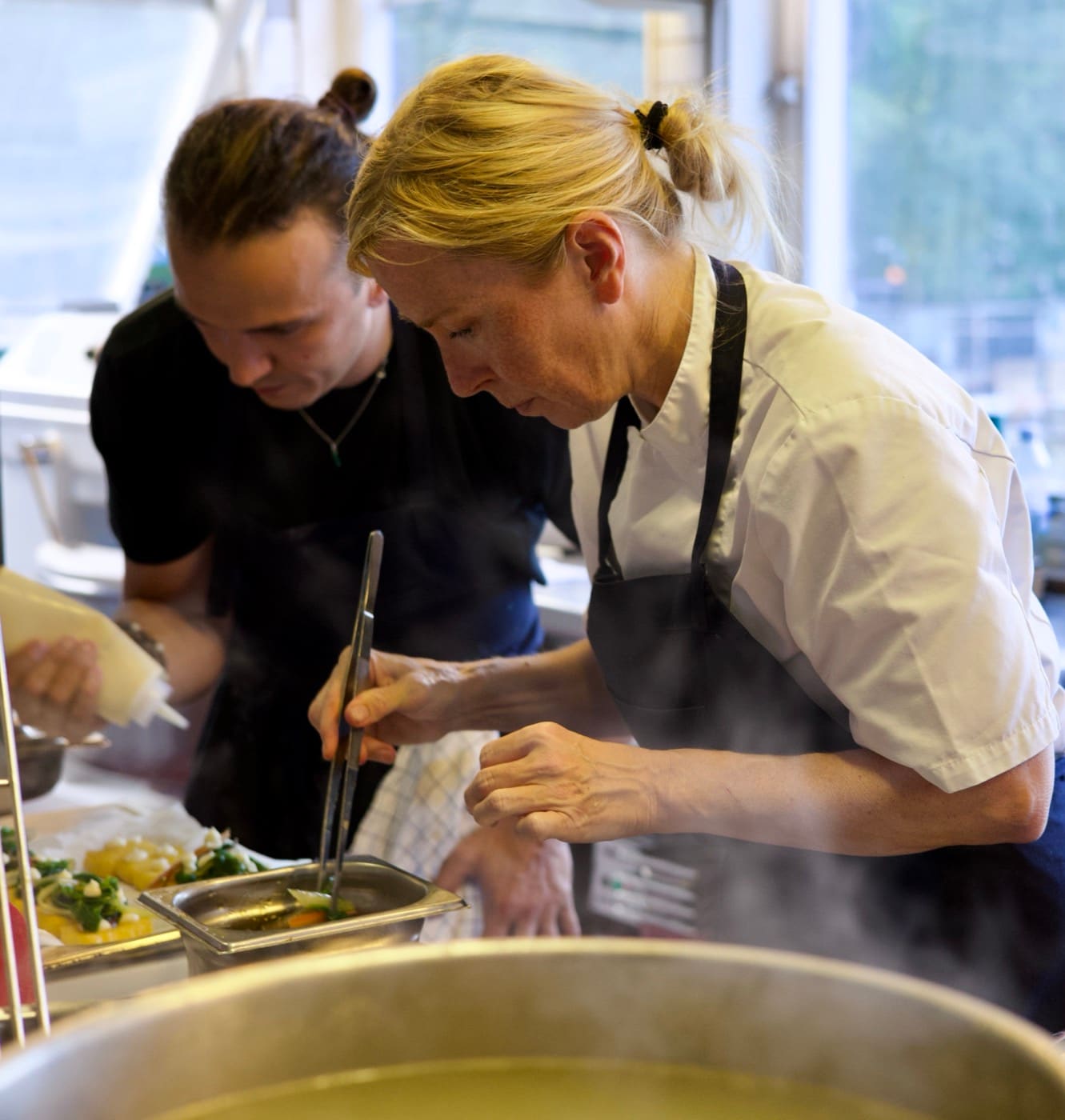 Two chefs plating in a steamy kitchen