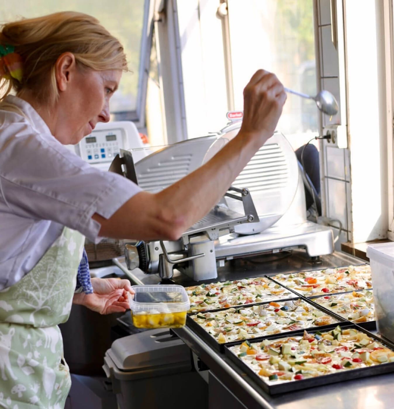 Pizza trays being topped in the kitchen